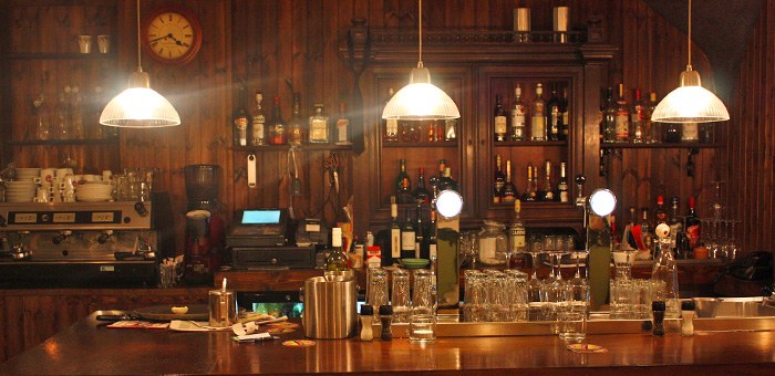 De houten bar met hanglampen en een goed gevulde drankenkast